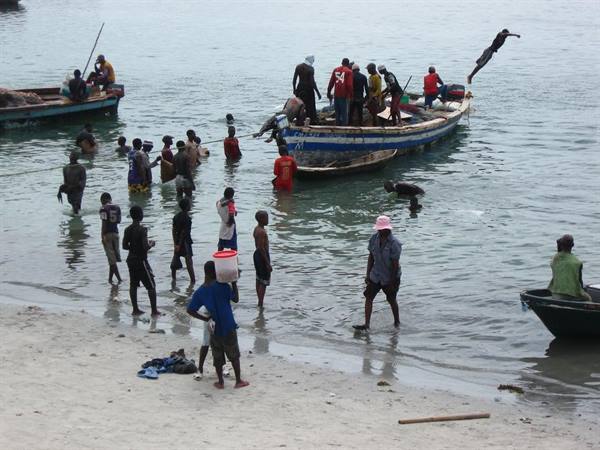 Fishermen and wooden boats on the beach, people wading with buckets