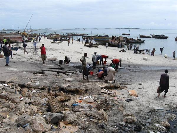Fishermen and wooden boats on the beach, people working among rocks and debris