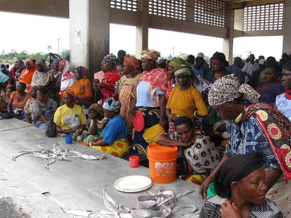 Women in colorful dresses selling fish at concrete counter under covered market
