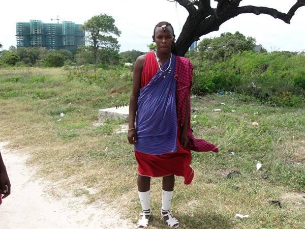 Young Maasai man in red and blue garments on grassy dirt path