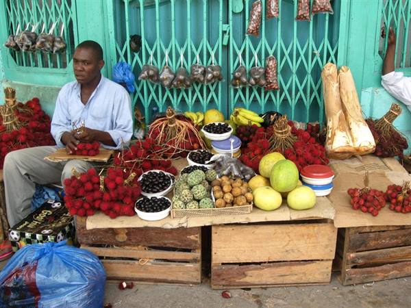 Fruit vendor before green gate: rambutan, bananas, pomelo on wooden crates