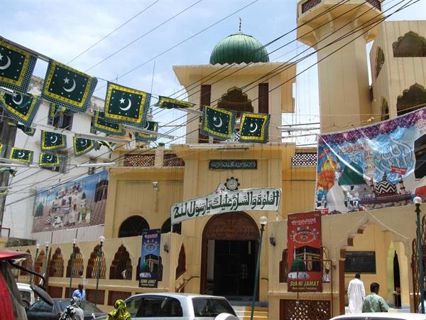 Mosque with green dome and Pakistani flags strung above a busy street