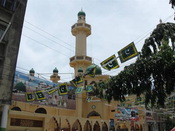 Cream minaret with green domes among crescent flags and power lines