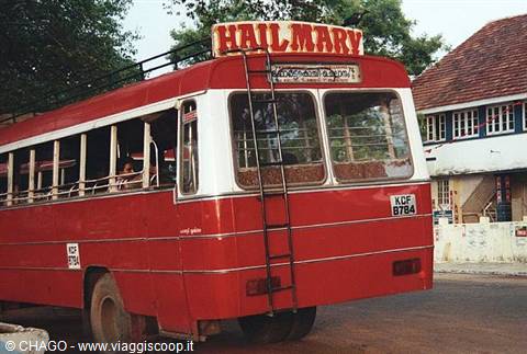 Red Hail Mary bus with yellow sign and metal ladders by a colonial house