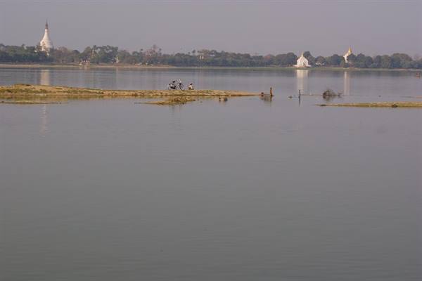 Man with motorcycle on a sandy strip in the lake, white pagodas on the shore