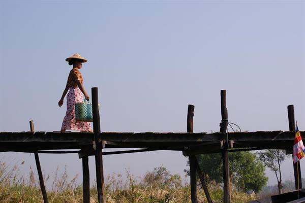 Woman in straw hat crossing an old teak wood footbridge