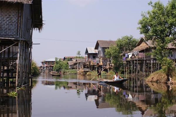 Man rows a boat past wooden stilt houses on Inle Lake