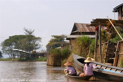 Women in straw hats on wooden boats, stilt houses at Inle Lake