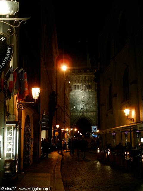 Cobblestone street at night with lit lanterns toward Prague's gothic tower