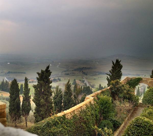 Cypress trees and stone wall above Tuscan hills under a stormy sky