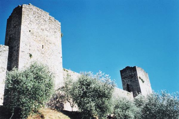 Ancient stone towers among olive trees under a blue sky