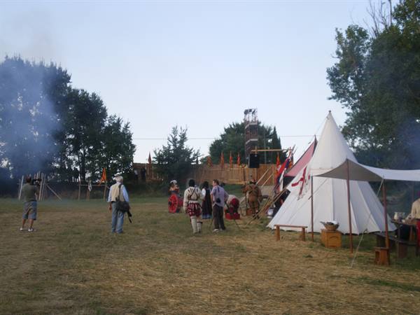 Historical reenactment: white canvas tent, flags and costumed people on dry grass