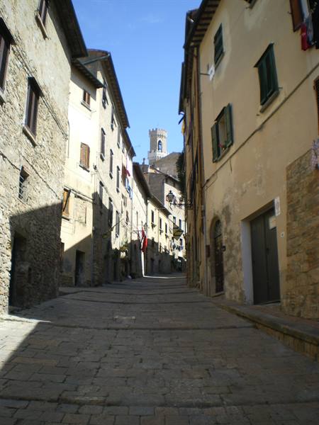 Cobbled uphill street between stone houses, tower in the distance