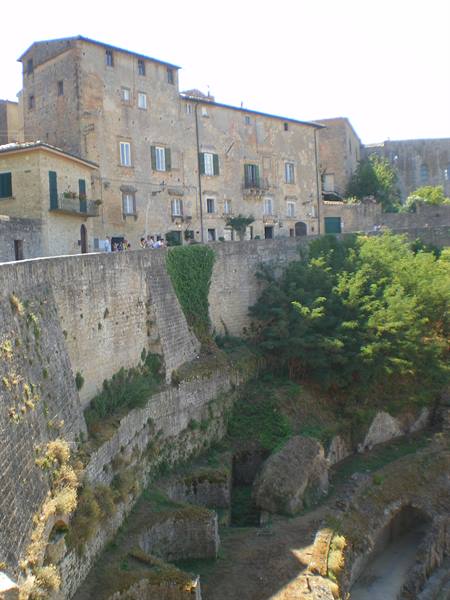 Pitigliano: tuff houses on carved slopes, ancient walls and tourists in sunlight