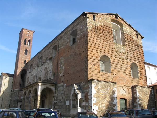 Romanesque brick and stone church with bell tower, parked cars under blue sky