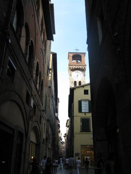 Busy street in Lucca, clock tower rising between brick buildings