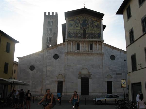 Cyclists ride past the marble facade and mosaic of San Frediano, Lucca