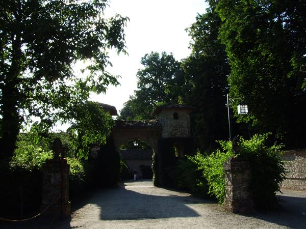 Stone gate entrance with arch and small tower, shaded tree-lined path