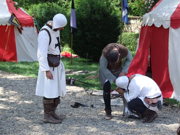 Medieval reenactment: men in white cross tunics among red and white tents
