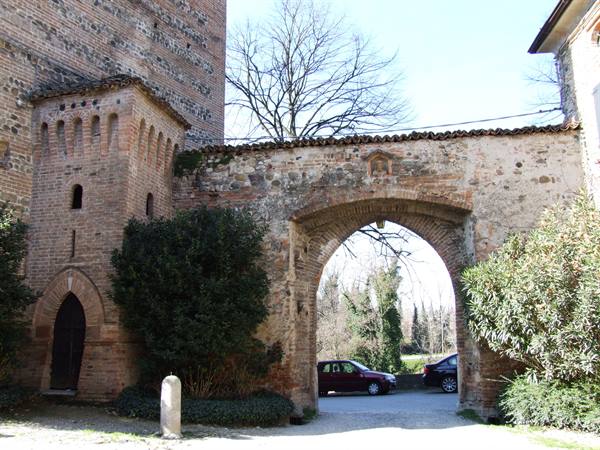 Old brick gate with arch, cars parked beneath, sunny light
