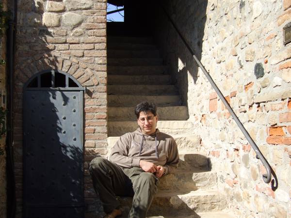 Man sitting on stone staircase between brick walls, iron door