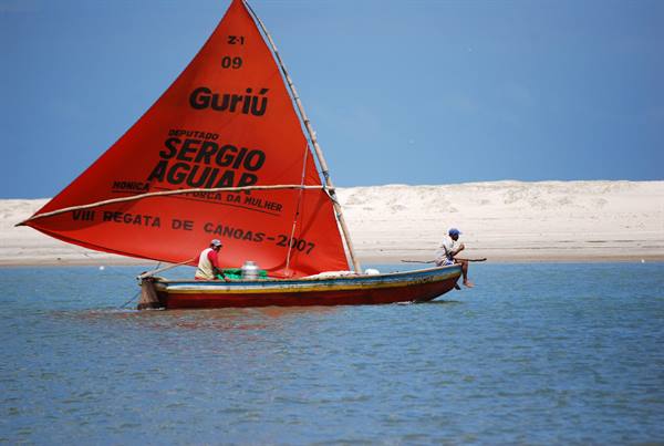 Jangada sailboat with red Guriú sail, two fishermen near the sand dune