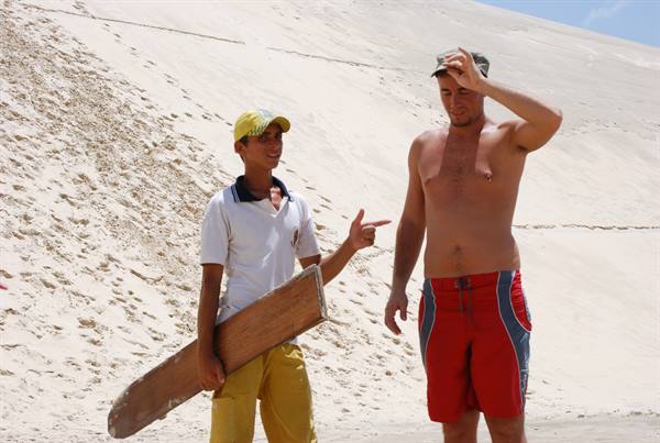 Boy with wooden sandboard and tourist on the white dune