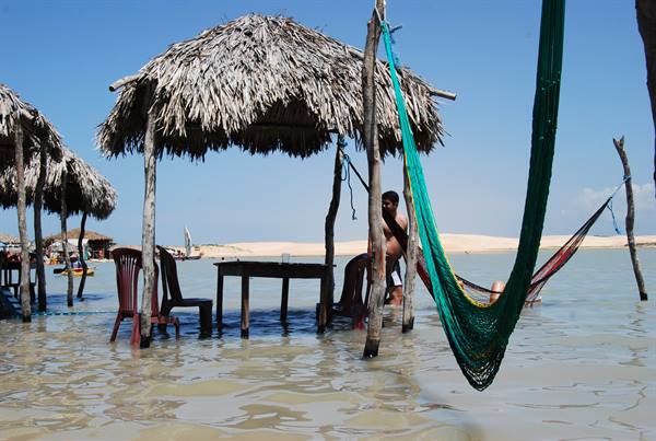 Green hammocks and tables standing in shallow water under thatched umbrellas at Jericoacoara