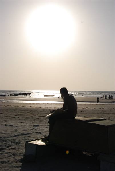 Silhouette of man sitting on wooden boat, people swimming on backlit beach