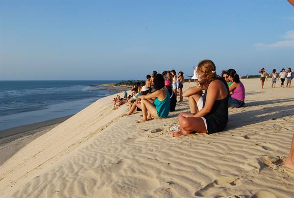 Tourists sitting on the sand dune facing the ocean at Jericoacoara