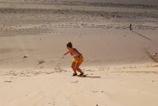 Woman in yellow sandboarding down a huge dune's soft sand