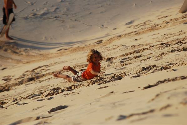 Little girl in red shirt slides down the sandy dune in warm light