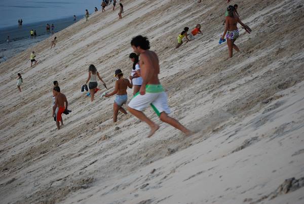Young people run and slide down the large sand dune toward the beach