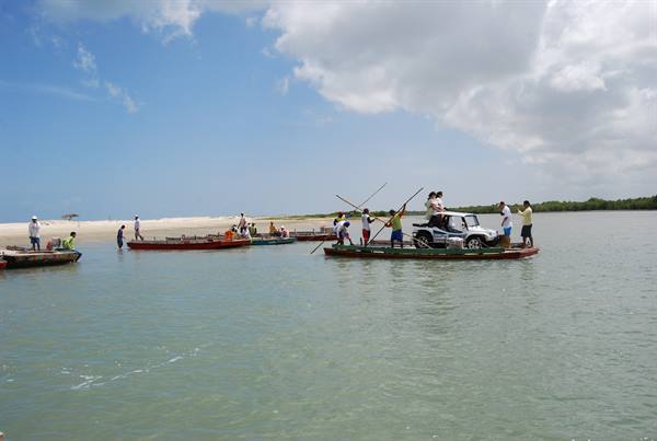 Wooden ferry raft carries a dune buggy across the water toward the beach