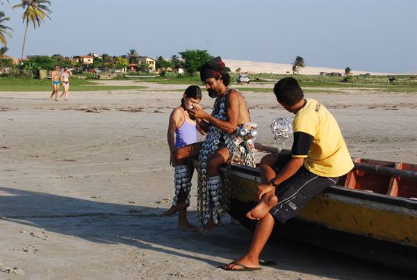 Man in shell costume shows phone to two boys on a boat at the beach