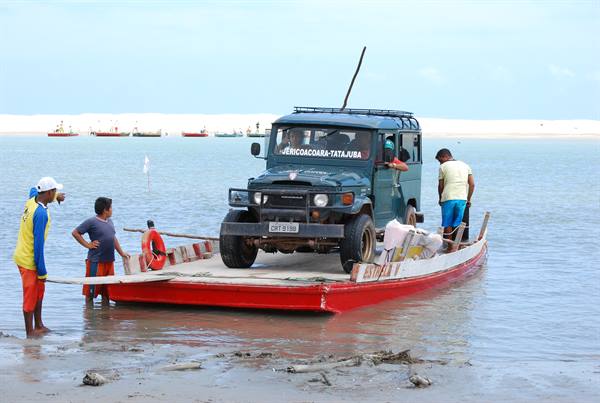 Toyota Bandeirante loaded on red wooden ferry, men standing in shallow water