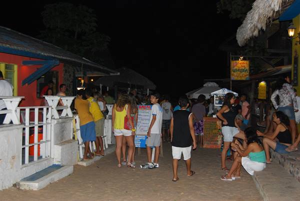 Tourists in summer clothes stroll at night among stalls and sandy beach bars