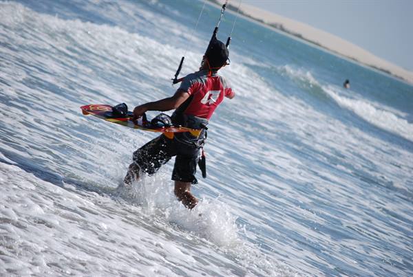 Kitesurfer in helmet carrying red board wades through white foam