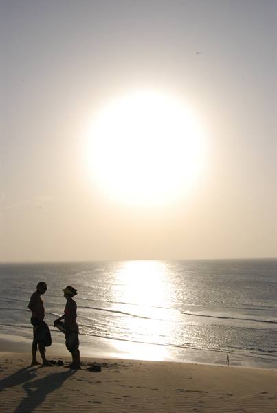 Two people silhouetted talk on the sand in front of the sea