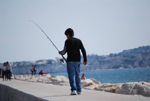 Boy fishing with rod from stone breakwater overlooking the bay