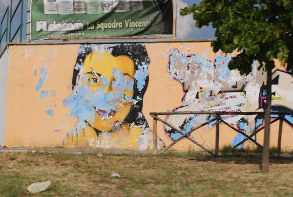 Faded female face mural on orange wall, torn posters and wooden fence
