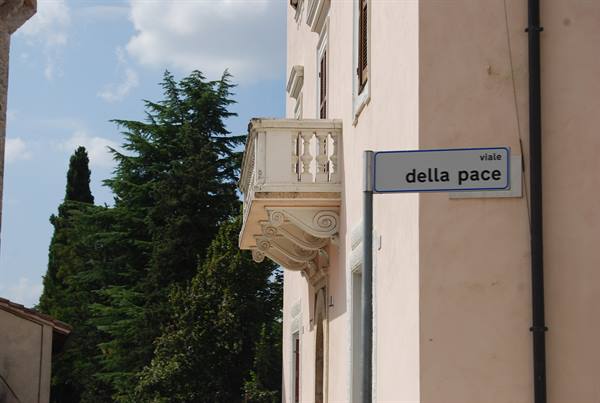 Street sign viale della Pace on pink building with stone balcony and cypresses