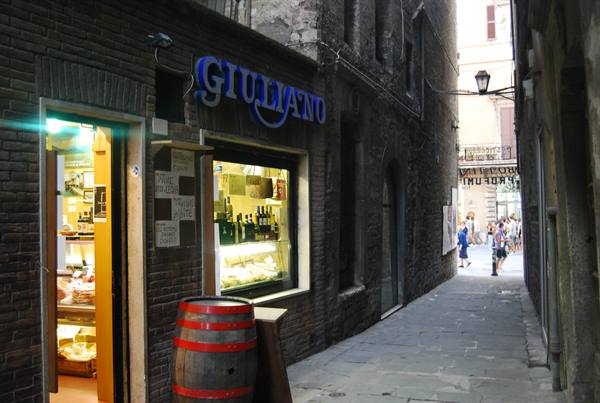 Giullano shop in a narrow brick alley, wooden barrel in front of the lit counter
