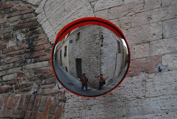 Red convex mirror on stone wall reflecting two people in an alley
