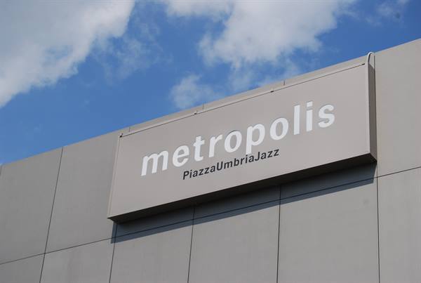 White Metropolis PiazzaUmbriaJazz sign on grey facade, blue sky with clouds