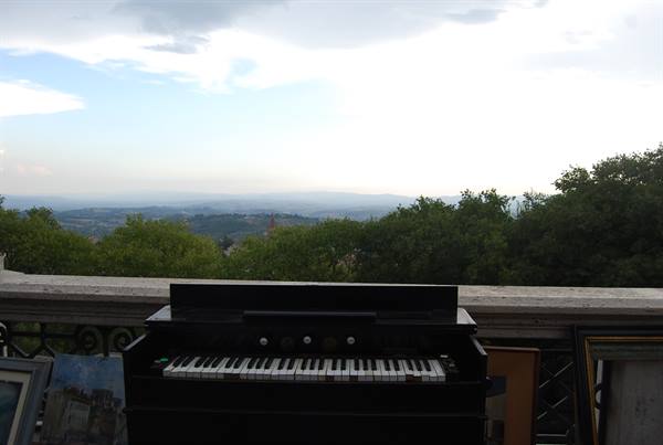 Black keyboard on a marble-railed terrace, green hills and cloudy sky behind