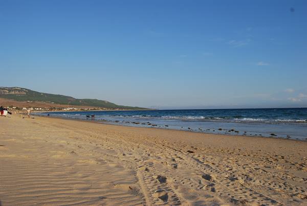 Footprints in the sand, ocean waves and green hills at Tarifa