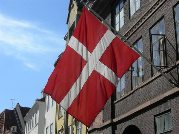 Danish flag waving in front of a dark brick building, blue sky