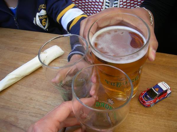 Kronenbourg beer glasses clinking on a wooden table with a toy rally car