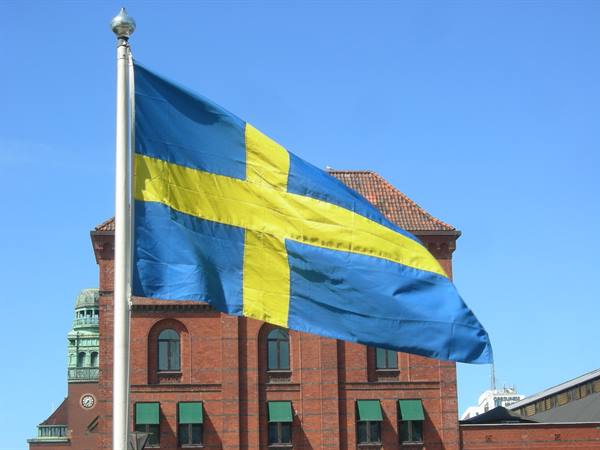 Swedish flag waving in front of a red brick building in Malmö
